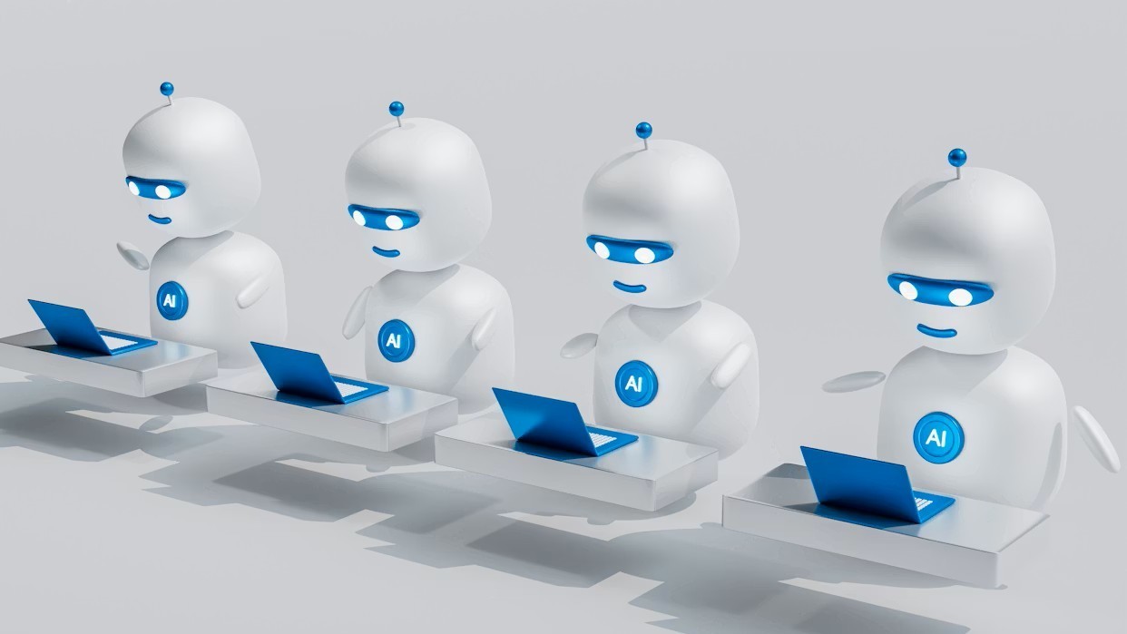 Four identical white robots with blue laptops sitting in a row.